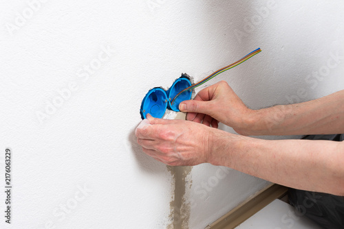 Skilled electrician carefully places blue flush-mount boxes into a wall opening, preparing for a new double electrical outlet installation in an apartment during home improvement