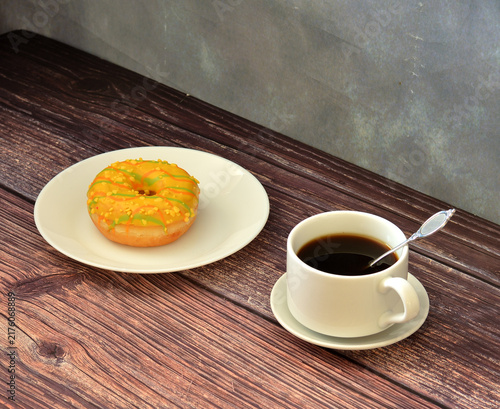 Konstfotografi A fresh doughnut with yellow linoleum filling and topping and a cup of hot black coffee on a wooden table