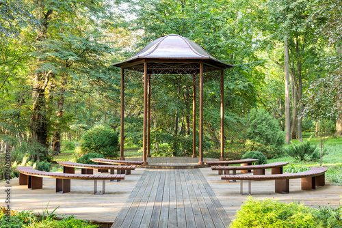фотографія Metal gazebo with benches and wooden deck in green park during daylight