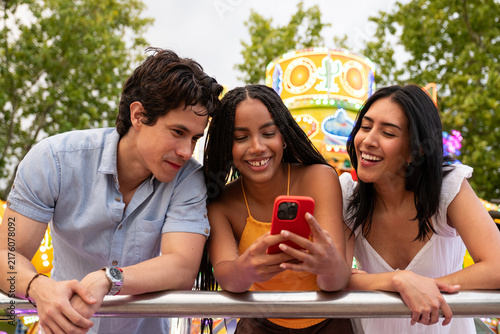 Group of diverse friends laughing while watching content on a smartphone at a fair