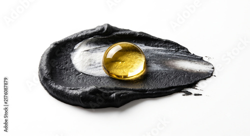 Macro shot of charcoal and kaolin clay swatch with golden yuzu oil drop on white background