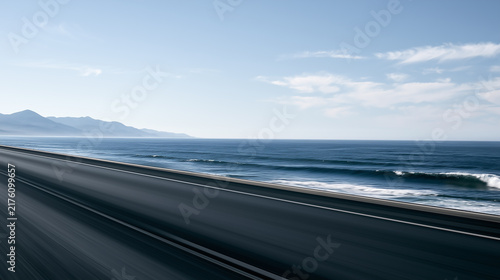An asphalt road stretching along the coastline with rough blue sea waves on the right and distant mountains in the background.