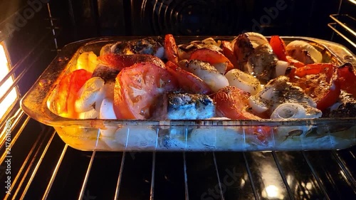 Roasting fish and fresh vegetables in a glass dish inside a domestic oven, healthy homemade dinner, Mediterranean diet, culinary process.
