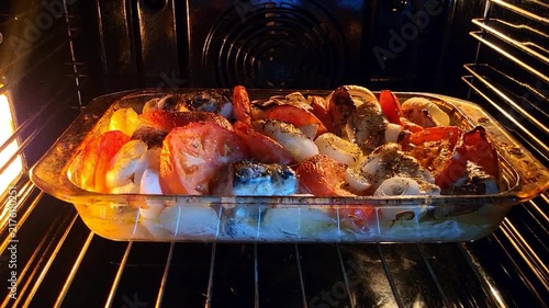 Close up of roasted fish with tomatoes and peppers baking in an oven, delicious healthy meal, savory dinner preparation, home cooking.