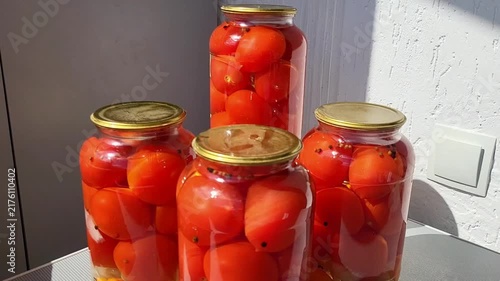 Multiple glass jars of preserved red tomatoes standing on a table, traditional home canning, winter food storage, organic harvest.