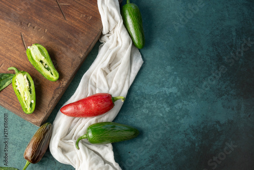 Obraz na plátně Green and red, jalapeno chili peppers on dark green background with a white cloth and wooden board