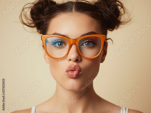 Close-up portrait of a playful young woman wearing orange glasses and puckering her lips.