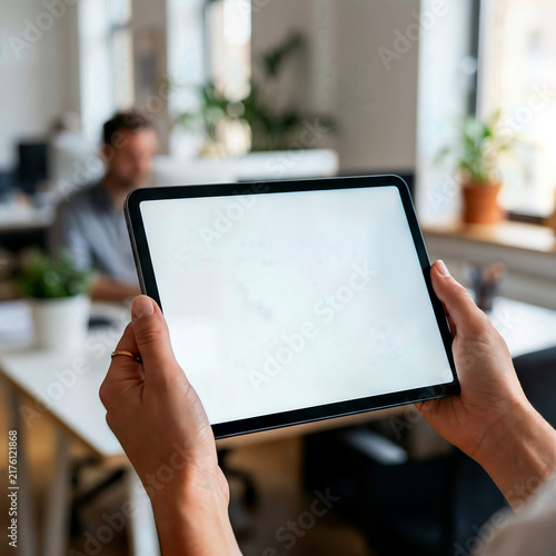 Person holding digital tablet with blank white screen in office