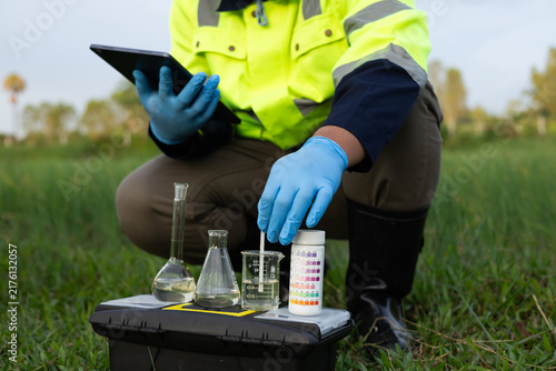 Environmental technician using a tablet with a portable water testing kit in an agricultural field.