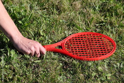 Photography Hand holding a red tennis racket above fresh green grass, active outdoor recreat