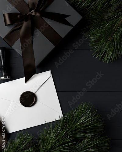 Luxury Christmas stationery scene with black gift box, sealed white envelope, evergreen branches and dark wood, styled for elegant masculine holiday designs.