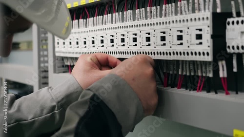 Close-up of technician wiring an industrial electrical control panel, connecting cables and working with electrical components inside a control cabinet.