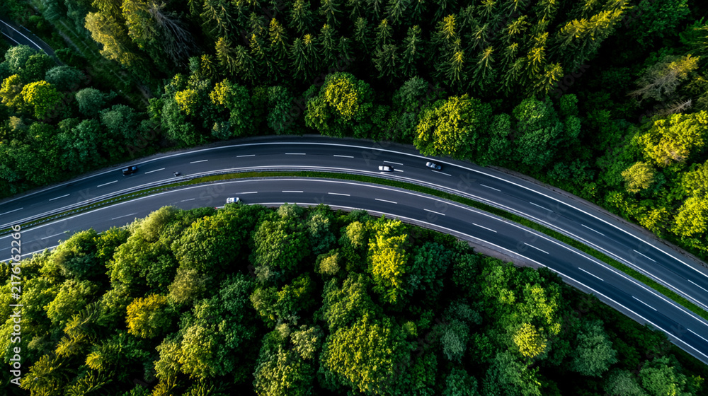Obraz premium Aerial view of a winding road through lush green forests, showcasing the beauty of nature as vehicles travel along the route, highlighting the intersection of forest and roadway.