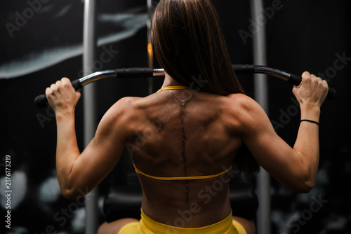 Fotografie Muscular woman performing lat pulldown exercise in gym from behind
