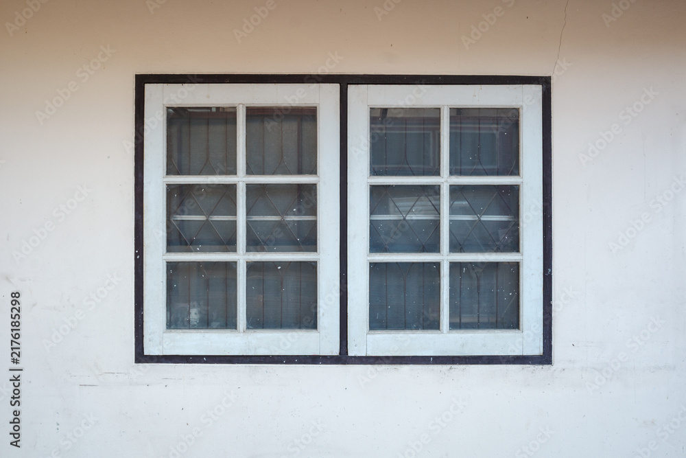 Fototapeta premium Close-up view of a classic white wooden window with multiple glass panes set into a plain concrete wall.