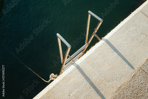 Concrete pier edge with metal ladder leading into deep blue water