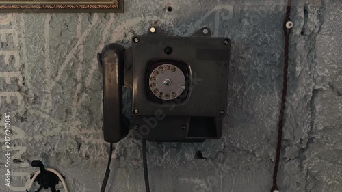Old vintage Soviet industrial rotary telephone mounted on a grunge grey concrete wall inside an authentic retro communication room handheld orbiting arc shot capturing historical cold war details