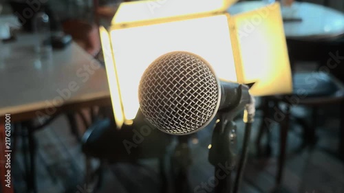 Professional dynamic microphone on stand with cinematic rack focus to bright LED video light panel inside empty cafe interior during documentary interview preparation handheld orbiting arc b-roll shot