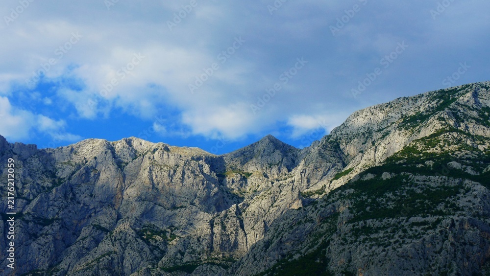 Obraz premium Big mountain peak scene with sun light and white clouds on a blue sky, mountain landscape background