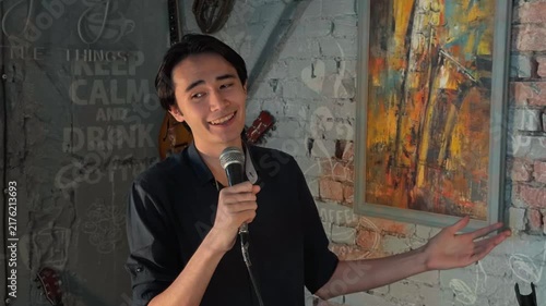 Candid Handheld Shot of Young Asian Spiritual Leader Preaching Sermon with Passionate Gestures Holding Microphone on Stage during Evening Church Gathering in Modern Cozy Cafe Authentic Lifestyle