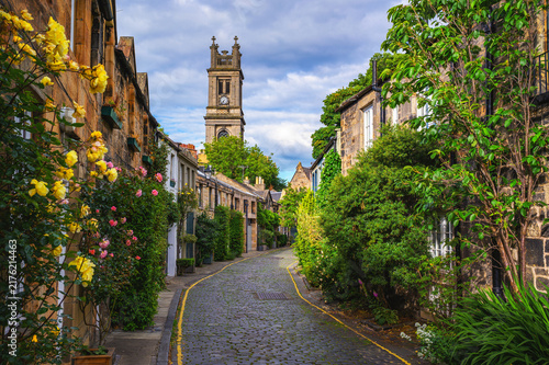 Cobblestone Circus Lane in Stockbridge  Edinburgh  lined with stone cottages  roses  and greenery  leading toward St Stephen s Church tower in Scotland  United Kingdom.