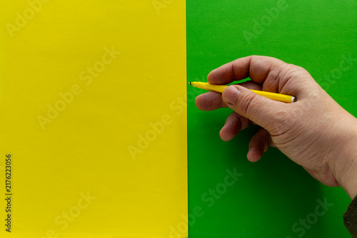 Foto Hand Holding Yellow Pen Over Split Yellow And Green Paper Background For Design