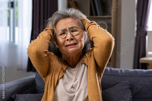 Obraz na plátne Elderly Asian woman holding her head with eyes closed, expressing stress and dis