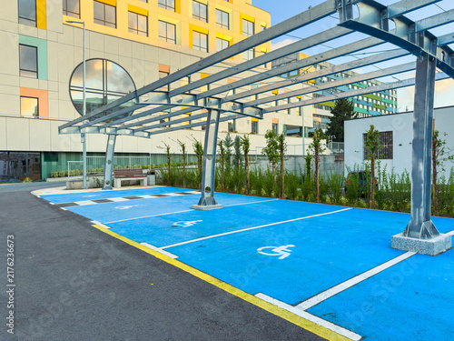 Parking area with marked spots under a structure for shade located in an urban environment during daylight hours