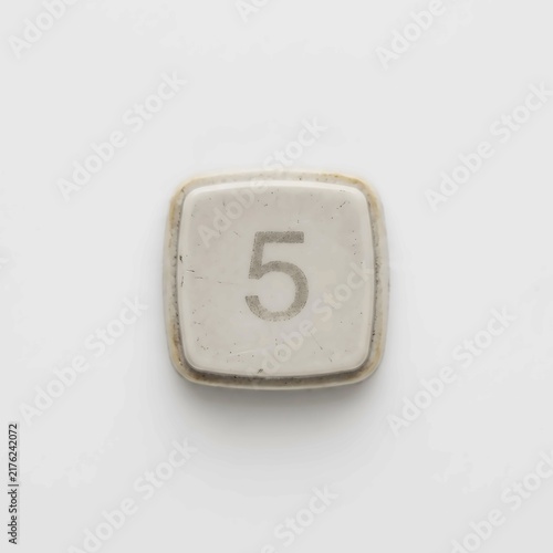 Vintage white typewriter key featuring the number five displayed in a simple clean font against a plain light gray background