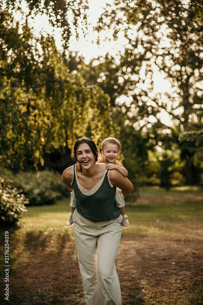 Fototapeta premium Mother giving piggyback ride to child in summer park