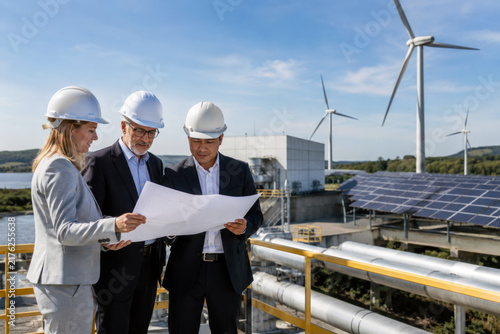 Multinational executives inspect renewable energy infrastructure while reviewing plans at a modern facility. International investment in cleaner and more sustainable development