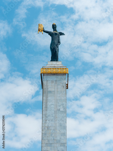 View of the Medea Statue holding the Golden Fleece atop a tall marble column against a blue sky with light clouds in Batumi, Adjara, Georgia.