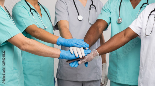 Diverse medical team in scrubs stacking gloved hands together, showing unity and teamwork