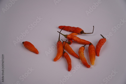 Fotografía Bright orange chilies are scattered over a plain white surface.