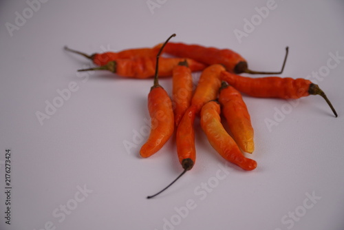 Obraz na plátně Bright orange chilies are scattered over a plain white surface.