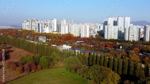 Aerial view of modern city with residential buildings and large green park in autumn. Urban skyline, colorful trees and green space show balance between city life and nature.