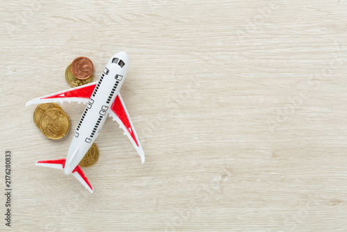Model of airplane with coins on wooden background, top view