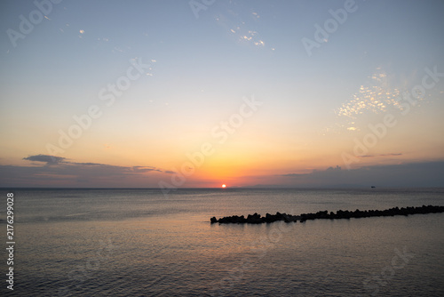 Fototapeta 水平線に太陽が沈む夕暮れの海とテトラポットのシルエット