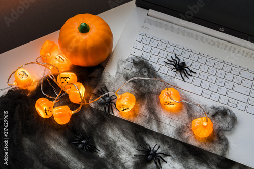 Halloween decorated home office with a laptop, glowing pumpkin lights, spider web and spiders, creating a spooky seasonal workspace for autumn and holiday content.