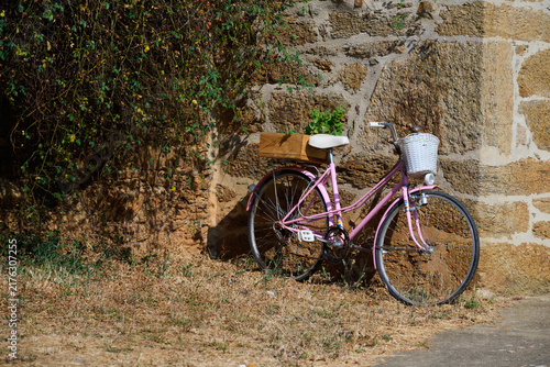 Pink vintage bicycle resting against rustic stone wall