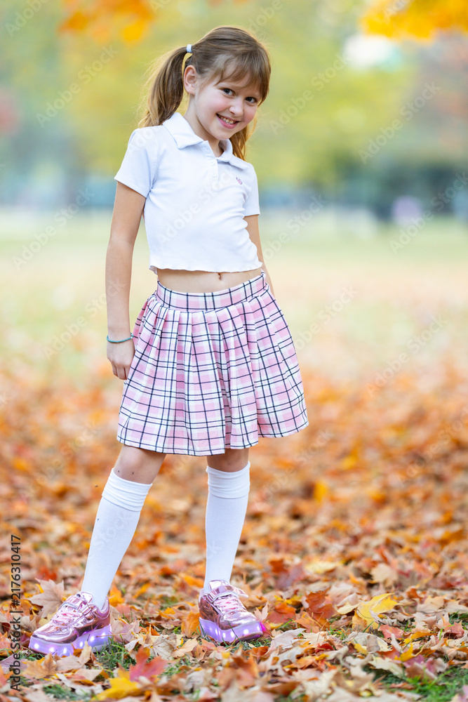 Obraz premium Autumn girl smiles with confidence. Autumn little girl holds foliage. Vibrant autumn background appears. Charming autumn child portrait.