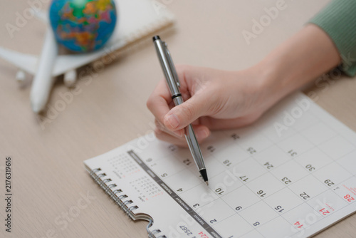 Travel, vacation planning concept. Person writing a trip schedule on a calendar with airplane model and globe for vacation preparation at home. Travel, planning, itinerary, vacation, tourism