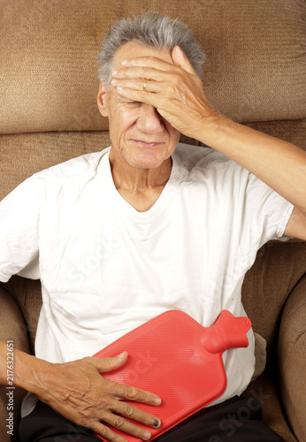 Older Man Applying a Hot Water Bottle on his stomach for pain relief  