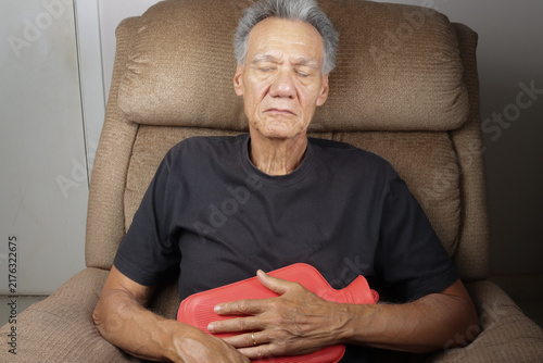 Older Man Applying a Hot Water Bottle on his stomach for pain relief  