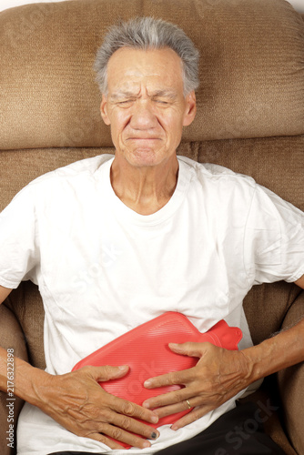 Older Man Applying a Hot Water Bottle on his stomach for pain relief  