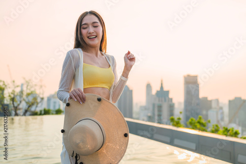 Картината върху платно Playful joyful young woman laughing with closed eyes holding straw hat at rooftop pool sunset, enjoying vacation bliss, freedom, luxury leisure, wellbeing, and cheerful vitality