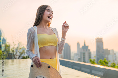 Obraz na płótnie Playful joyful young woman laughing with closed eyes holding straw hat at rooftop pool sunset, enjoying vacation bliss, freedom, luxury leisure, wellbeing, and cheerful vitality