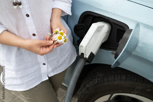 Woman holding daisy flowers while charging an electric car