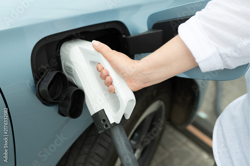 Close up of a white charging connector inserted into the socket of a light blue electric car. Concept of eco friendly transportation, alternative energy source, and modern EV charging station infrastr