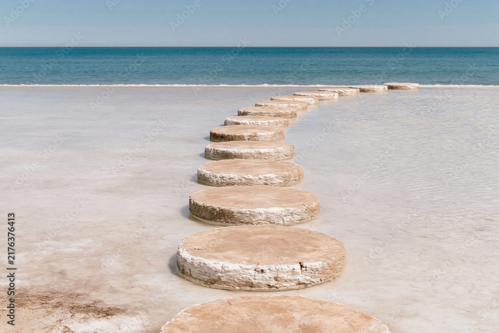Obraz premium Circular stepping stones forming a path across still, pale water toward a distant horizon for a personal journey and progress campaign